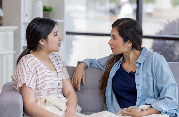 Teen and adult sitting on couch talking.