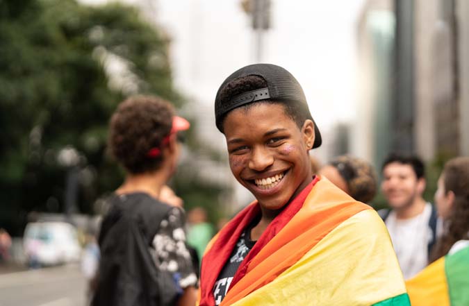 Teen wearing baseball hat with rainbow flag wrapped around his shoulders