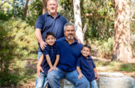A couple and their sons smiling, surrounded by trees.