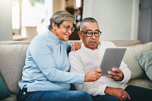 A couple sits on a couch and smiles as they look at an ipad