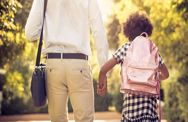 A daughter wears a backpack and holds her father's hand as they walk