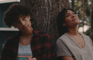 Teenage boy and adult woman sitting with their backs to a tree and looking up at the sky