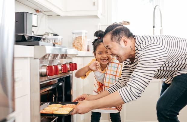 An adult and child laugh as they bake cookies in the kitchen 