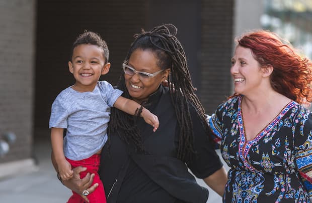 A couple walking and smiling, looking at their child