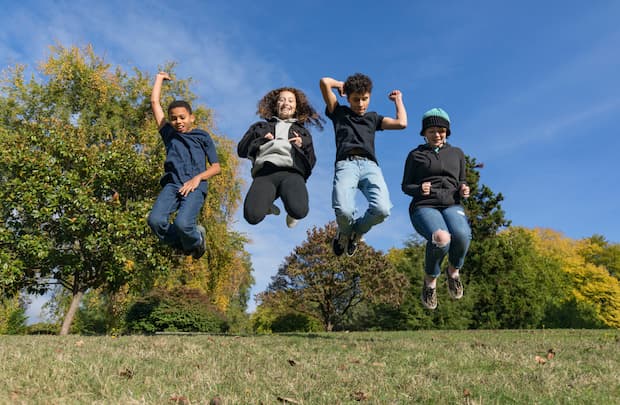 4 smiling teenagers shown jumping in mid air on a sunny day in the park