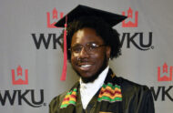 Tyler Hunter Boards smiling while wearing a cap and gown and standing in front of a wall that says "WKU"