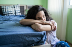 Woman with dark hair sitting on the floor and leaning on a bed