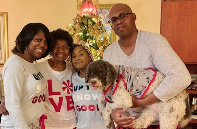 Family posing in front of a Christmas tree while wearing holiday pajamas 