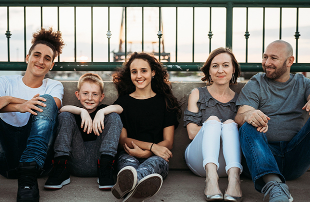 Ahgren family of five leans against bridge for family photo.