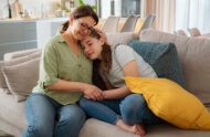 Mother comforting teenage daughter while sitting on couch.