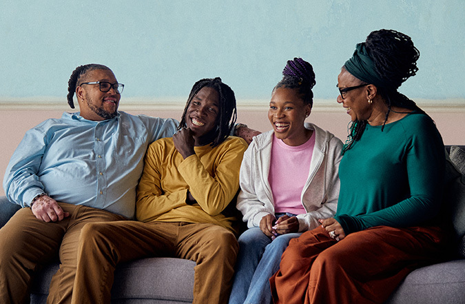 A family of four laughs together on a couch. The Jones family participated in both the 2023 and 2024 PSA campaign, and this image of their family will appear in various ads throughout the year. Seated from left to right are James, Za'Quan, Princess, and Keeshann. 