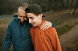 A father puts his hand on his son's shoulder as they walk together outside.