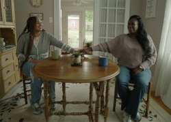 A young woman and her mom sit across from each other at a dining table and hold hands.
