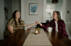 Mother and daughter, Erin and Emma, smile and hold hands across a dining table.