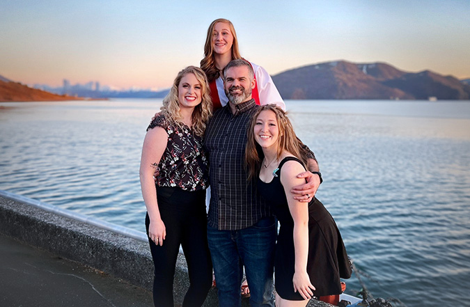 The Hagelman family poses for a photo in front of a body of water and mountains.